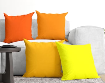 Op de afbeelding: Een set van vier vierkante sierkussens in een levendig kleurverloop. De collectie bestaat uit een feloranje kussen, een medium oranje kussen, een goudgeel kussen en een neongeel kussen, allemaal met een gladde, effen afwerking.
