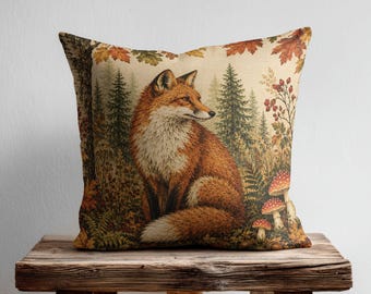 May include: A square throw pillow featuring a printed illustration of a red fox sitting in a forest. The scene includes evergreen trees, autumn leaves, and red mushrooms with white spots. The background is a light beige colour with forest details.
