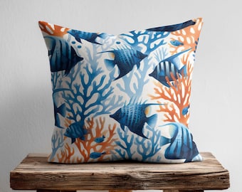 May include: A square throw pillow featuring a repeating pattern of dark blue striped angelfish swimming among vibrant orange and light blue coral branches on a white background. The design covers the entire front surface of the pillow.