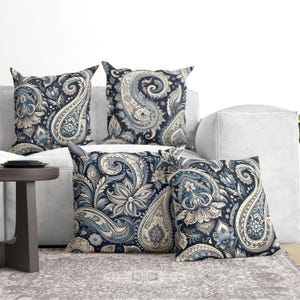 Peut inclure: Quatre coussins carrés ornés d'un motif cachemire détaillé dans des tons bleu marine, bleu clair et crème. Le design complexe comprend des formes de gouttelettes tourbillonnantes, des motifs floraux et des éléments botaniques imprimés.
