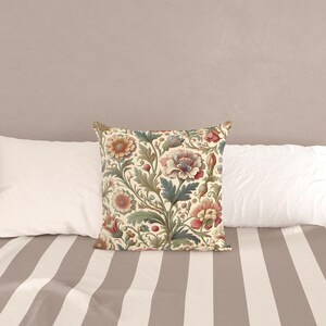 May include: A square throw pillow featuring a cream-colored background with a dense, repeating botanical pattern of stylized flowers and leaves in muted shades of pink, dusty blue, sage green, and deep red, arranged in a flowing, intricate design.