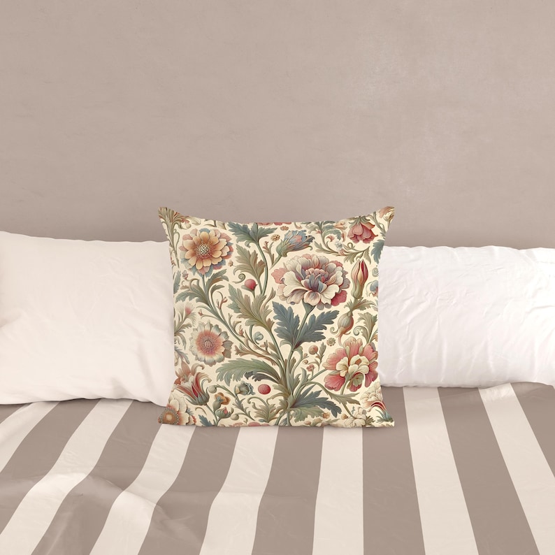 May include: A square throw pillow featuring a cream-colored background with a dense, repeating botanical pattern of stylized flowers and leaves in muted shades of pink, dusty blue, sage green, and deep red, arranged in a flowing, intricate design.