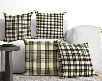 May include: Four square throw pillows featuring a plaid pattern in shades of cream, black, and grey. The pillows are arranged in a group, each displaying a consistent grid-like design with intersecting horizontal and vertical lines of varying thickness.