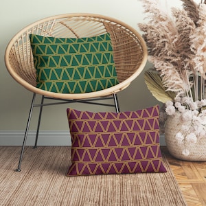 May include: Two decorative throw pillows with a geometric pattern of gold triangles on a green and burgundy background. The pillows are sitting on a wicker chair and a brown rug.