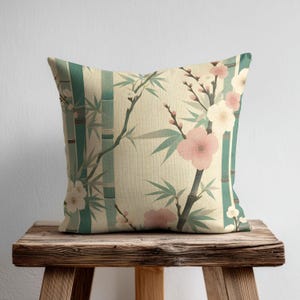 Peut inclure: Un coussin carré avec un fond crème orné d'un motif répétitif de tiges de bambou verticales bleu sarcelle, de feuilles de bambou vertes et de fleurs de cerisier rose pâle et blanches sur toute la surface du tissu.