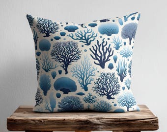May include: A square throw pillow featuring a repeating pattern of various coral and seashell illustrations in shades of navy and light blue on an off-white background. The design displays diverse marine life shapes including branching coral and rounded sea sponges.