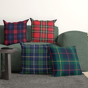 May include: Four square throw pillows featuring various plaid patterns. One pillow has a red and navy blue tartan, another is bright red with green and yellow lines, one is green and navy blue, and the last is dark green with red and yellow.