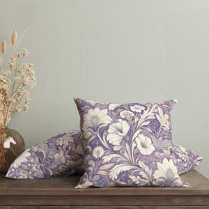 May include: Two decorative throw pillows with a floral pattern in shades of purple and cream. The pillows are on a wooden surface.