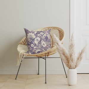May include: A wicker chair with a throw blanket and a purple floral pillow. A vase with dried pampas grass sits on the floor next to the chair.