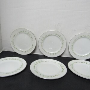 May include: Set of six white ceramic dinner plates with a green floral design around the edge.