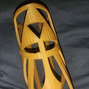 Puede incluir: Un brazalete de plástico amarillo dorado impreso en 3D con un diseño triangular.