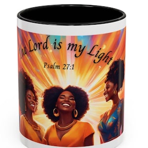 May include: White ceramic mug with a black rim. The mug features a colorful illustration of three women with bright smiles and a quote that reads "The Lord is my Light, Psalm 27:1".
