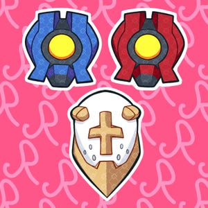 May include: Three stickers featuring stylised designs. Two stickers are symmetrical, shield-like shapes in blue and red, each with a central yellow circle. The third sticker is a white, pointed shield shape with a gold cross and two small tan horns.