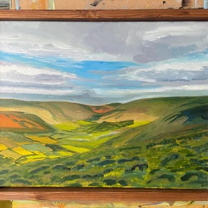 Könnte beinhalten: Ölgemälde einer Landschaft mit grünen Hügeln und Tälern unter einem bewölkten Himmel mit blauen Flecken. Das Kunstwerk ist in einem dunkelbraunen Holzrahmen gerahmt.