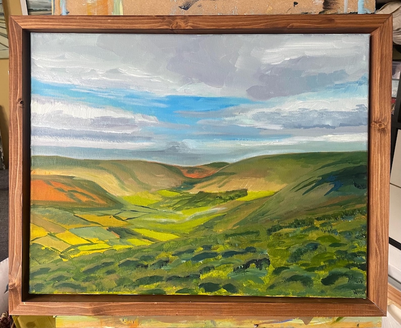 K&ouml;nnte beinhalten: &Ouml;lgem&auml;lde einer Landschaft mit gr&uuml;nen H&uuml;geln und T&auml;lern unter einem bew&ouml;lkten Himmel mit blauen Flecken. Das Kunstwerk ist in einem dunkelbraunen Holzrahmen gerahmt.