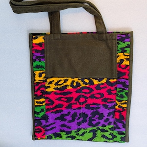 Könnte beinhalten: Olivgrüne Tragetasche mit farbenfrohem Leopardenmuster. Die Tasche hat einen einfarbigen olivgrünen Körper und Träger mit einem lebendigen Leopardenmuster in Pink, Gelb, Lila und Grün. Die Tasche ist aus robustem Stoff gefertigt.