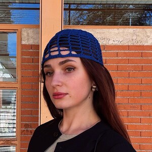 Peut inclure: Un chapeau bleu crocheté avec un motif en forme de grille. Le chapeau est porté par une personne. L'arrière-plan présente un mur de briques et une fenêtre. Le chapeau est un accessoire élégant.