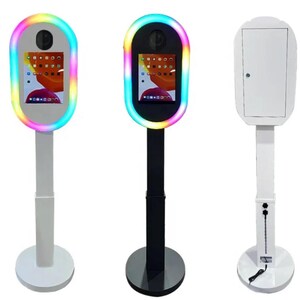 May include: Three photo booth stands, one with a white frame and white stand, one with a black frame and black stand, and one with a rainbow-colored frame and white stand.