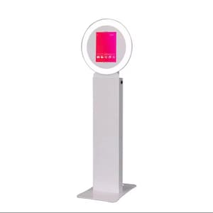 May include: White photo booth with a ring light and a touch screen display. The screen shows a pink and red gradient with icons for taking photos and videos.