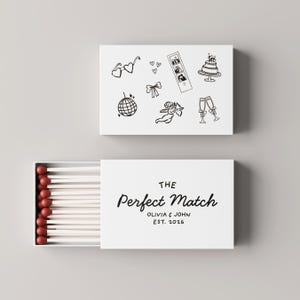 Peut inclure: Une boîte d'allumettes blanche avec le texte "THE Perfect Match OLIVIA & JOHN EST. 2026". La boîte est ouverte, révélant des allumettes à bout rouge. Le dessus de la boîte présente des dessins au trait noirs sur le thème du mariage.