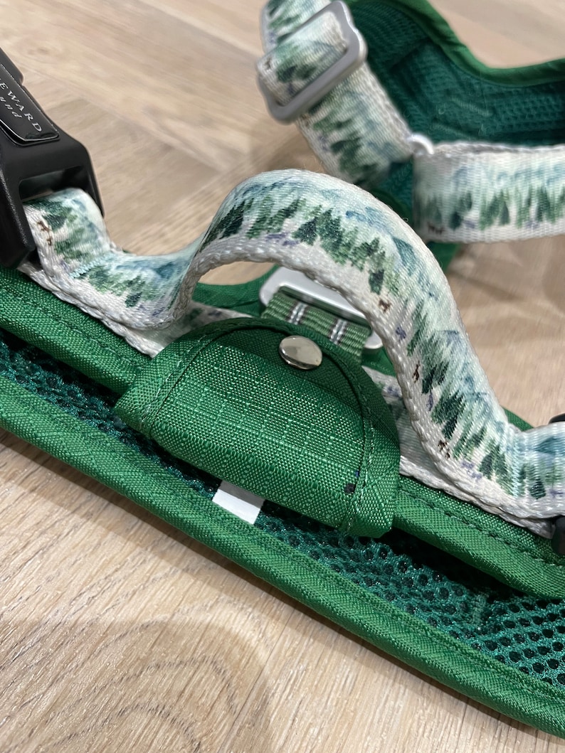 May include: Green dog harness with a white strap featuring a forest print. The harness has a black buckle with the word "REWARD" printed on it.