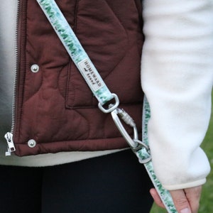 Puede incluir: Una correa para perro de color blanco y verde con un clip plateado. La correa tiene el texto "Homeward Bound" impreso en ella.