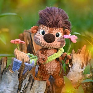 May include: A crocheted hedgehog plush toy with brown yarn fur, a dark brown nose, and large black eyes. It has a tuft of dark brown hair on its head, holds a light green vine, and stands next to a small blue basket containing pink flowers.
