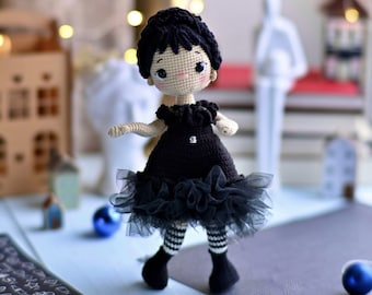 May include: A crocheted doll wearing a black dress with a tulle skirt and black and white striped stockings. The doll has black hair and brown eyes.