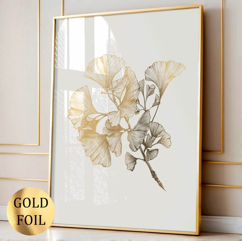 May include: A framed wall art print featuring a detailed botanical illustration of ginkgo biloba leaves in a metallic gold foil finish against a plain off-white background. The artwork is encased in a thin gold-colored metal frame.