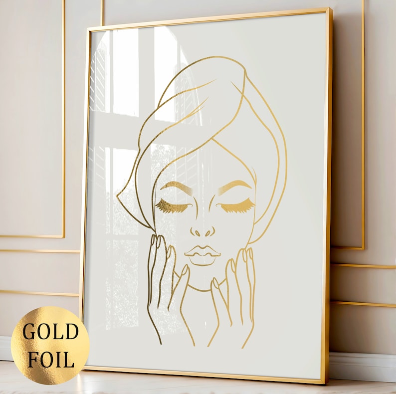 May include: A gold foil line art print of a woman with her eyes closed and hands on her face. The woman is wearing a towel on her head.