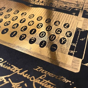 Peut inclure: Gros plan sur un clavier de machine &agrave; &eacute;crire couleur or avec les touches &eacute;tiquet&eacute;es avec des lettres et des chiffres. L'inscription "Inventor:  Latham Sholes" est visible en bas de l'image.