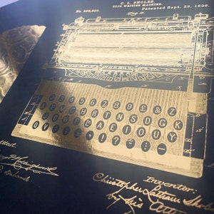 May include: A black and gold vintage typewriter patent drawing with the text "No. 868,830. C. L. SHOLES. TYPE WRITING MACHINE. Patented Sept. 29, 1896. Fig. 2." and the keys labeled with letters and numbers.
