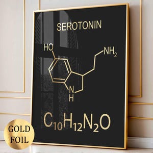 Może przedstawiać: Prostokątny obraz ścienny z czarnym tłem, przedstawiający strukturę chemiczną serotoniny w kolorze złotej folii, słowo SEROTONIN oraz wzór chemiczny C10H12N2O. Wydruk jest oprawiony w cienką złotą ramę, widoczna jest również naklejka ze złotej folii.
