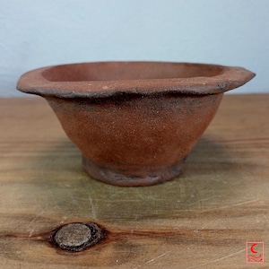 Könnte beinhalten: Eine kleine, handgeformte Terrakotta-Schale mit einem rustikalen, unebenen Rand und einer texturierten, matten rotbraunen Oberfläche. Die Schale hat eine breite, ausgestellte Öffnung, die sich zu einem schmalen, runden Boden hin verjüngt.