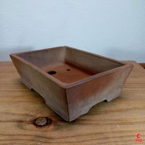 Peut inclure: Un pot à bonsaï rectangulaire de couleur brun rougeâtre. Le pot a un design légèrement effilé et un petit trou de drainage. Fabriqué en céramique, il est idéal pour les bonsaïs. Le pot mesure environ 25 cm de long.