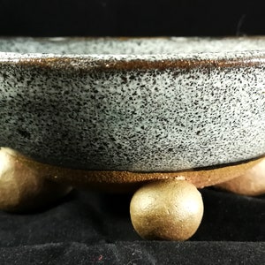 Könnte beinhalten: Ein weißer Keramik-Bonsai-Topf mit einem gesprenkelten Überzug und einem braunen Rand. Der Topf hat vier abgerundete Füße in Goldfarbe.