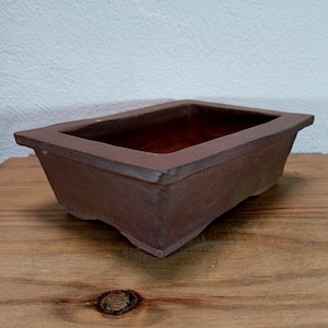Może przedstawiać: Prostokątna, brązowa doniczka ceramiczna do bonsai z lekko uniesionym rantem i gładkim, matowym wykończeniem.