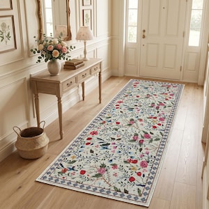 May include: A long rectangular runner rug featuring a cream-colored background with a vibrant floral pattern of pink, red, and yellow flowers, green leaves, and small blue birds, finished with a dark blue and white geometric border design.