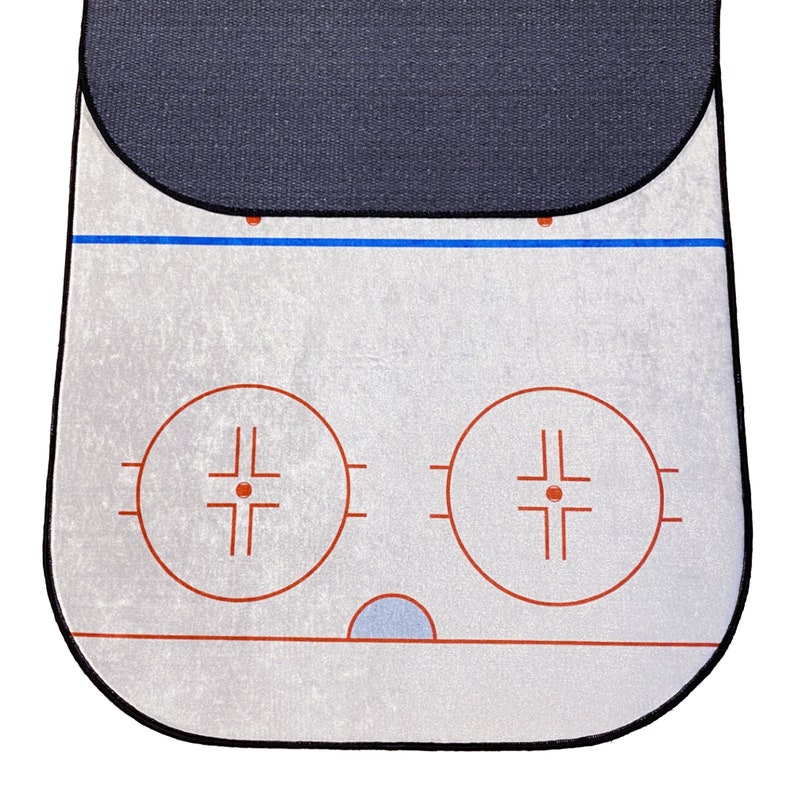 May include: A white hockey shooting pad with two red circles and a black border. The circles have a red crosshair design inside. The pad has a blue line across the top and a black border around the edges.
