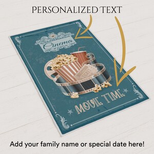 Puede incluir: Un letrero de tem&aacute;tica cinematogr&aacute;fica de color verde azulado con las palabras "Cinema" y "Movie Time". El letrero presenta palomitas de ma&iacute;z, una bebida y una bobina de pel&iacute;cula. El texto "Personalized Text" est&aacute; en la parte superior y "Add your family name or special date here!" en la inferior.