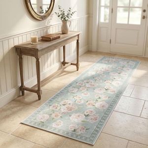 May include: A long rectangular runner rug featuring a light sage green background with a repeating pattern of soft pink and white roses. The rug has a decorative border with a geometric diamond pattern along the edges, creating a floral design.