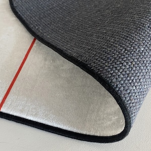 May include: Close-up of the back side of a rug with a black border and a white, plush surface. A red line runs along the edge of the rug.