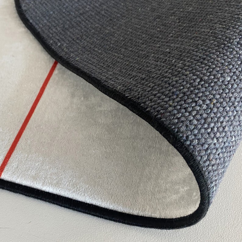 May include: Close-up of the back side of a rug with a black border and a white, plush surface. A red line runs along the edge of the rug.