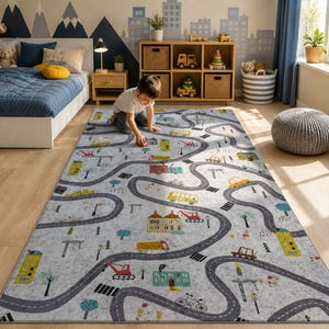 May include: A gray road-themed play rug with winding roads, buildings, and vehicles. The rug features a light gray background with dark gray roads, and colorful illustrations of cars, trucks, and buildings. A child is playing with a toy car on the rug.