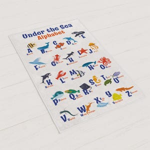 May include: A rectangular, white educational rug featuring the "Under the Sea Alphabet." Each letter is paired with a colorful sea creature illustration. The rug is designed for children and educational purposes.