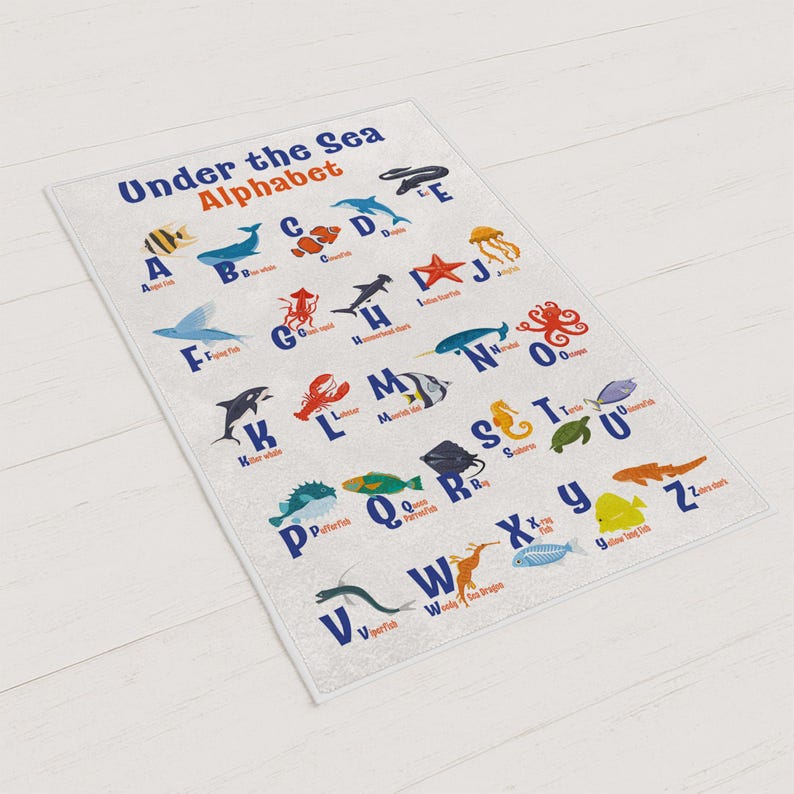 May include: A rectangular, white educational rug featuring the "Under the Sea Alphabet." Each letter is paired with a colorful sea creature illustration. The rug is designed for children and educational purposes.