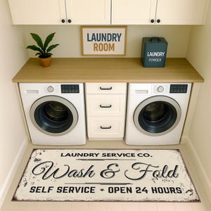 May include: A laundry room featuring two white washing machines, a wooden countertop, and a sign that reads "LAUNDRY ROOM." A metal sign on the floor says "Wash & Fold, Self Service Open 24 Hours."