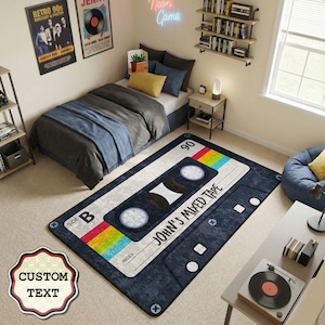 Può includere: Un tappeto rettangolare a forma di musicassetta, con la scritta "JOHN'S MIXED TAPE". Il tappeto ha uno sfondo blu scuro con dettagli bianchi e arcobaleno. La stanza comprende anche un letto, poster e un giradischi.