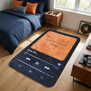 Puede incluir: Una alfombra rectangular diseñada para parecerse a una interfaz de reproductor de música. La alfombra presenta un borde negro y un centro naranja texturizado con el texto "ALBUM COVER HERE". Debajo, muestra los controles de la canción y el texto "Song Title Artist 2:23".