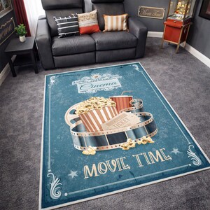 Puede incluir: Alfombra rectangular azul con tem&aacute;tica de cine. La alfombra presenta una cubeta de palomitas de ma&iacute;z, un vaso de bebida, una bobina de pel&iacute;cula y una entrada de cine. Las palabras "Cinema" y "Movie Time" tambi&eacute;n se muestran.